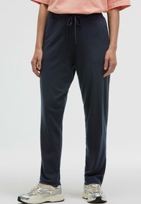 Marineblaue Jogginghosen mit einem Kordelzugbund, hergestellt aus weichem Stoff. Mit einem lockeren Schnitt und seitlichen Taschen, kombiniert mit hellen Sneakers.