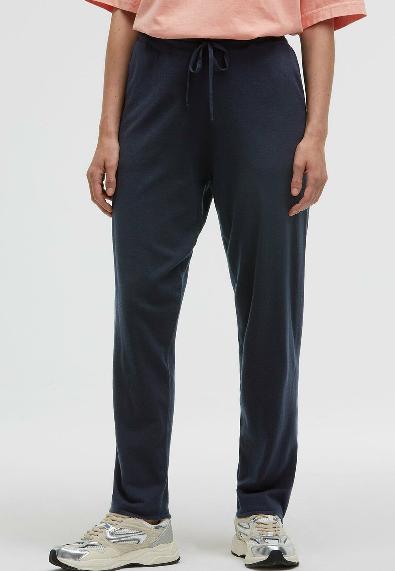 Marineblaue Jogginghosen mit einem Kordelzugbund, hergestellt aus weichem Stoff. Mit einem lockeren Schnitt und seitlichen Taschen, kombiniert mit hellen Sneakers.