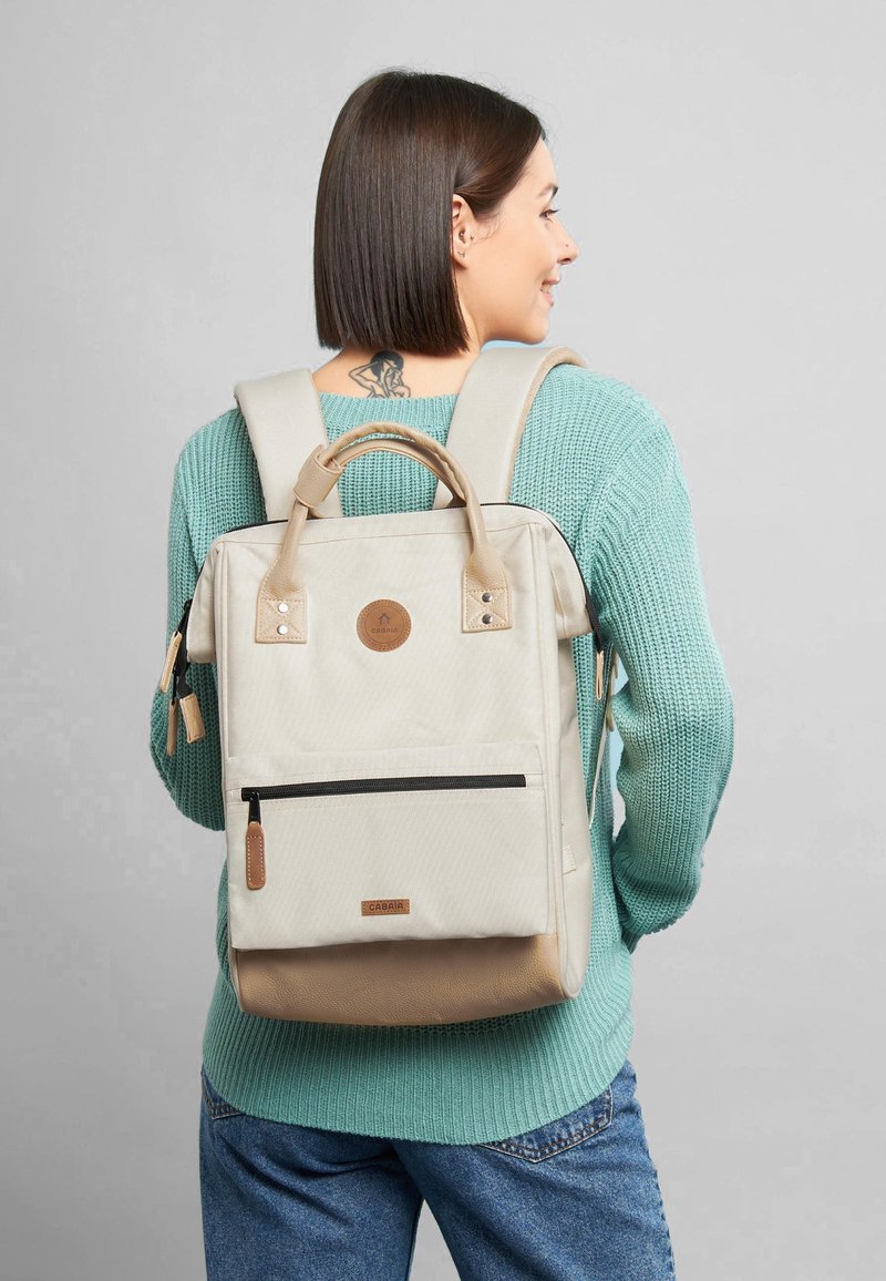 Cremefarbene Rucksack mit strukturiertem Finish, doppelten Oberhandgriffen, verstellbaren Trägern und einer vorderen Reißverschlusstasche. Mit einem Leder-Logo-Patch.