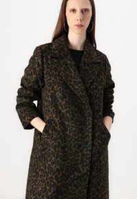 Manteau en imprimé léopard fabriqué en tissu doux, présentant une palette de couleurs vert foncé et marron, un col cranté et des poches latérales.