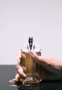 Gouden parfumfles met een transparante, diamantachtige dop en slanke silhouet. Hand die de basis vastgrijpt, geaccentueerd door lange, netjes verzorgde nagels.