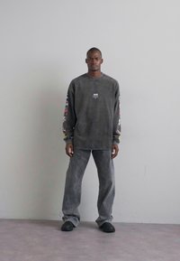 Grey oversized sweatshirt with long sleeves featuring colorful graphics, paired with matching grey loose-fit pants and black footwear.