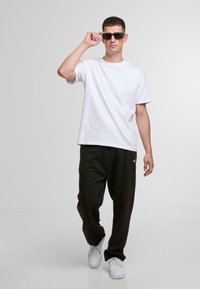 White cotton t-shirt, black sweatpants with vertical seams, and white sneakers. Individual wearing black sunglasses, standing in a neutral background.