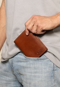 Pruun nahast rahakott, mis on osaliselt helesinise teksapoe taskust väljas. Rahakotil on sile tekstuur ja nähtavad õmbluse detailid.