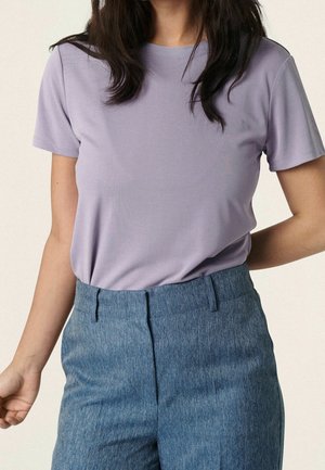 Jasnofioletowa koszulka z krótkim rękawem z miękkiej, gładkiej tkaniny, zestawiona z teksturowanymi, jasnoniebieskimi, wysokim stanem spodniami o prostym kroju.