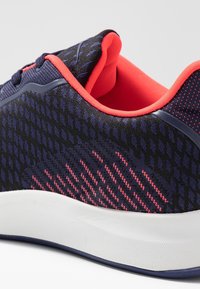 Námořnické sportovní boty s texturovaným síťovaným svrškem, červenými akcenty a bílou gumovou podrážkou s vlnitým vzorem. Navrženy pro pohodlí a podporu.