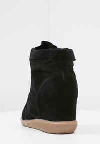 Baskets compensées en daim noir avec semelle en caoutchouc couleur marron clair vues de dos sur fond blanc.