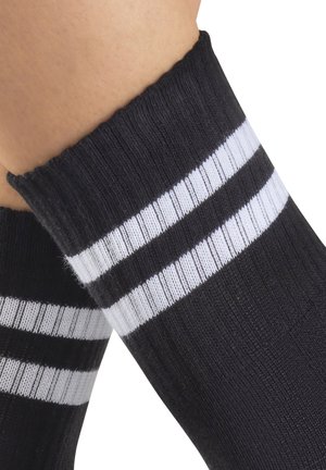 Black ribbed socks with two white horizontal stripes worn on a person's lower legs against a white background.