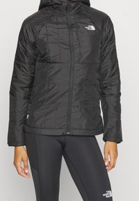 Svart isolerad jacka med huva, som har en kviltad design, framdragkedja och logotypdetalj på vänster bröst. Slät, glänsande material.