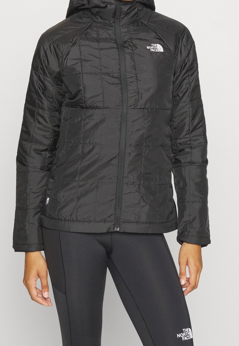 Svart isolerad jacka med huva, som har en kviltad design, framdragkedja och logotypdetalj på vänster bröst. Slät, glänsande material.