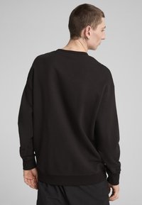 Sudadera negra con un corte holgado, puños y dobladillo acanalados, con una textura suave y un diseño minimalista. Incluye un cuello redondo.