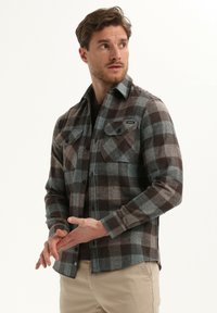 Bruine, grijze en blauwe geruite flanellen blouse met een button-down kraag, twee borstzakken en lange mouwen. Subtiel gemarmerde stof.