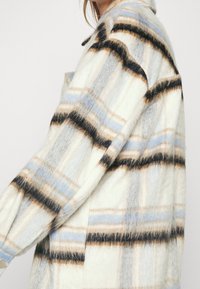 Chaqueta de cuadros de gran tamaño hecha de una tela suave; presenta rayas en azul, marrón y crema con un acabado texturizado y acentos de botones.