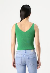 Groene geribbelde tanktop met een V-halslijn, slim fit ontwerp en brede banden, gecombineerd met lichtblauwe slim fit jeans. Gladde textuur, minimale details.