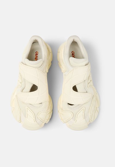 Krämfärgade sneakers med en strukturerad mesh-ovandel, utskuret mönster och en tjock, mönstrad sula. Har vadderade vristar och kardborreband.