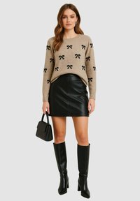 Maglione beige con motivi a fiocco neri, abbinato a una mini gonna in pelle nera. Stivali neri alti fino al ginocchio con tacco e una piccola borsa nera.