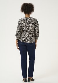 Zwart en crèmekleurig top met zebra-patroon en driekwartmouwen, gecombineerd met donkerblauwe skinny jeans en zwarte hoge hakken.