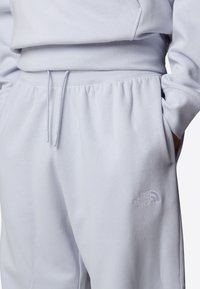 Ljust grå mjukisbyxor i mjukt material har en elastisk midja med dragsko, sidofickor och en subtil broderad logotypdetalj.