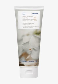 Valkoinen Kukka -vartalovoide 200 ml valkoisessa tuubissa. Ominaisuuksina pehmeä koostumus ja kukkakuvio, jossa on valkoisen kukan kuva ja sinistä tekstiä.