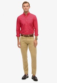 Czerwona koszula na guziki, khaki chinosy, pleciony brązowy pasek i ciemnobrązowe loafersy. Prosty design, gładka tekstura i dopasowany krój.