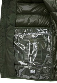 Interior de una chaqueta acolchada verde que presenta un bolsillo transparente para evidencias con etiquetas impresas y un logotipo en la esquina inferior izquierda.