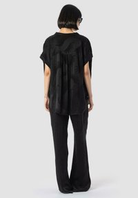 Črna oversize majica z subtilnimi ročnimi vzorci, v kombinaciji s črnimi širokimi hlačami. Obe izdelani iz mehke, strukturirane tkanine. Prikazan zadnji pogled.