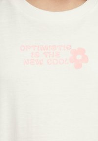 Witte katoenen T-shirt met roze tekst "OPTIMISTIC IS THE NEW COOL" en een roze bloemgrafiek. Soepele textuur en ronde halsontwerp.