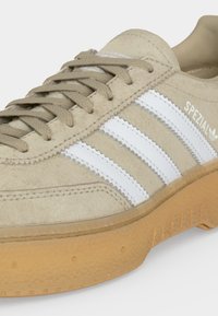 Baskets beige en daim avec trois bandes blanches et semelle en gomme, avec le logo "SPEZIAL" près de la cheville.