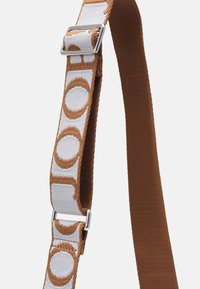 Brązowy pas z tkaniny z białym plecionym fragmentem ozdobionym okrągłymi wzorami. Metalowe okucia łączą pas, zwiększając jego wytrzymałość.