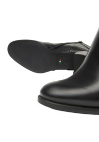 Stivale alla caviglia in pelle nera con texture liscia, chiusura con zip e suola in gomma piatta, contrassegnato da un'etichetta che indica "Fabbricato in Italia" e taglia 37.