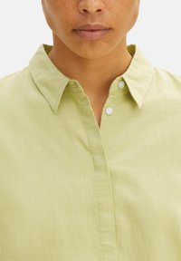 Camicia color verde chiaro con colletto, realizzata in un tessuto liscio, dotata di chiusura a bottoni e con un design pulito e semplice. Metti in evidenza il collo e i dettagli del tessuto.