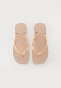 Bage flip-flopi z rjavo teksturirano podplatno in svetlo rjavimi sijočimi trakovi. Na traku je izbočen logotip "Calvin Klein Jeans".