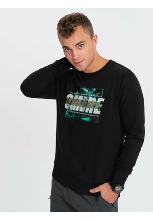Sudadera negra de manga larga con puños acanalados, que presenta un gráfico rectangular con el texto "OMBRE" en tono azul verdoso y plateado. Textura suave, corte casual.