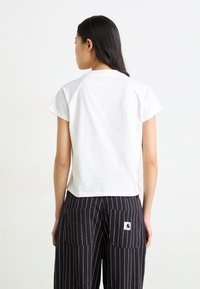 Hvid bomulds t-shirt med korte raglanærmer og en cropped pasform, båret med sorte nederdelbukser med striber og to baglommer.