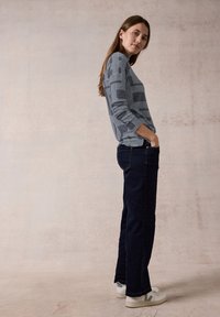 Maglione grigio e bianco con motivo geometrico, a maniche lunghe, abbinato a jeans a gamba dritta blu scuro e sneaker bianche.
