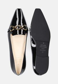 Ballerine in vernice nera con punta affusolata, caratterizzate da un accento in catena dorata e una fodera interna beige. Suola piatta con logo del marchio sulla parte inferiore.