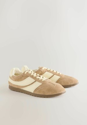 Braune Wildleder-Sneaker mit cremefarbenen Streifen und Schnürsenkeln, ausgestattet mit einem weichen Innenfutter und einer strukturierten Außensohle. Klassisches Retro-Design.