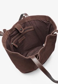 Brown suede bucket bag interior with a zip pocket, smooth brown leather strap, and soft fabric lining. Open top design with a snap closure.