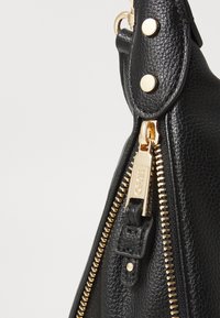 Black leather handbag featuring a textured finish, gold-tone zipper, and hardware accents. Includes a zippered closure and decorative studs.