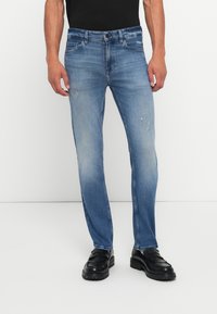 Blue denim jeans with a straight leg design, light wash, subtle distressing, five pockets, and standard button-and-zip closure.