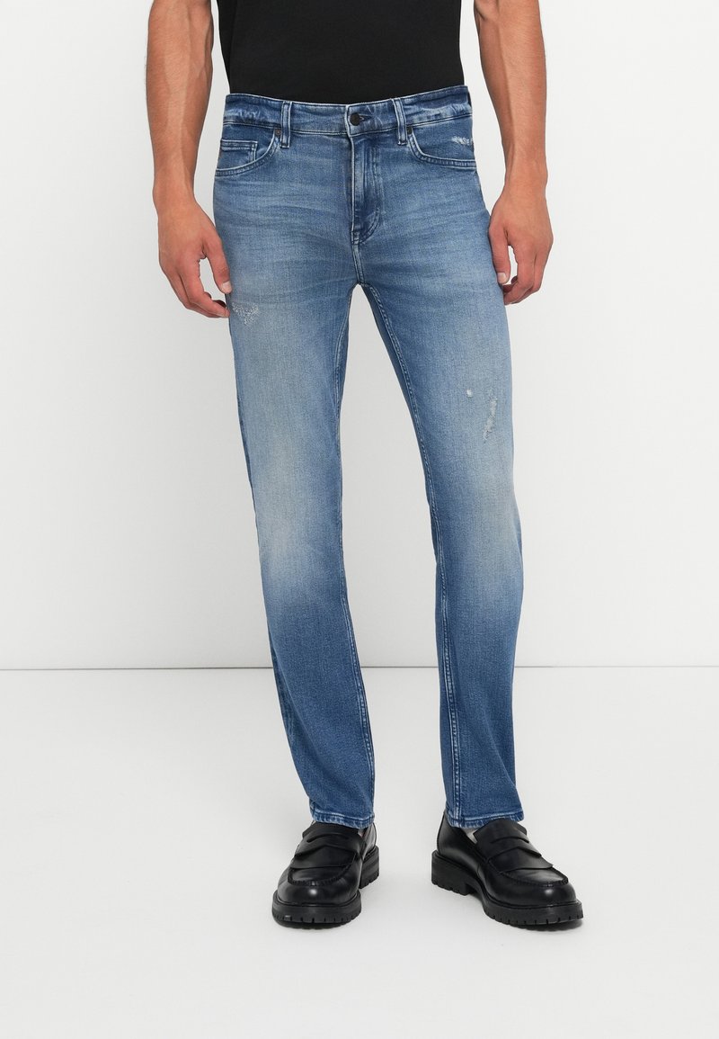Blue denim jeans with a straight leg design, light wash, subtle distressing, five pockets, and standard button-and-zip closure.