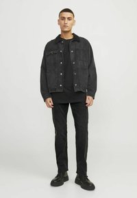 Svart denimjacka med fyra framfickor, knäppning med knappar och patchdetalj, buren över en svart skjorta och matchad med svarta jeans och skor.