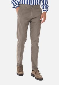Chinos in cotone beige con una vestibilità dritta, chiusura con zip, tasche laterali e una finitura lucida, abbinati a stivaletti marroni con lacci.
