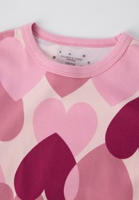 Lyhythihainen vaaleanpunainen paita, jossa on sydänkuvio eri vaaleanpunaisen ja burgundin sävyissä, pehmeällä neulepinnalla ja pyöreällä kaula-aukolla.