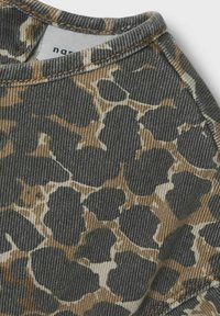 Vêtement gris avec un motif à pois dans des teintes noires et brunes. Présente un col côtelé et est fabriqué à partir d'un tissu texturé.