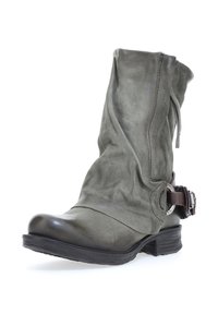 Botín de cuero verde hasta el tobillo con un diseño holgado, punta redondeada y detalle de correa marrón contrastante con una hebilla metálica. Superficie texturizada.