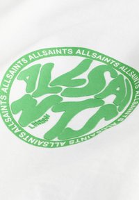 Grønt cirkulært logo på en hvid stofbaggrund, med stiliseret tekst "ALLSAINTS" og "LONDON" i fed skrift og med glat tekstur.