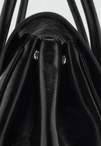 Sac seau en cuir noir avec une finition lisse et brillante. Il dispose d'une ouverture resserrée et d'accents en métal argenté pour la fermeture et les poignées.