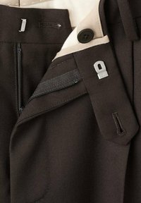 Pantaloni marroni in tessuto texturizzato; dotati di zip, chiusura con bottone e dettagli interni in tessuto. Inclusi accessori in metallo.