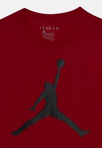 Κόκκινο βαμβακερό T-shirt με μεγάλο μαύρο λογότυπο Jordan. Στρογγυλή λαιμόκοψη με ετικέτα στο εσωτερικό της περιοχής του γιακά.